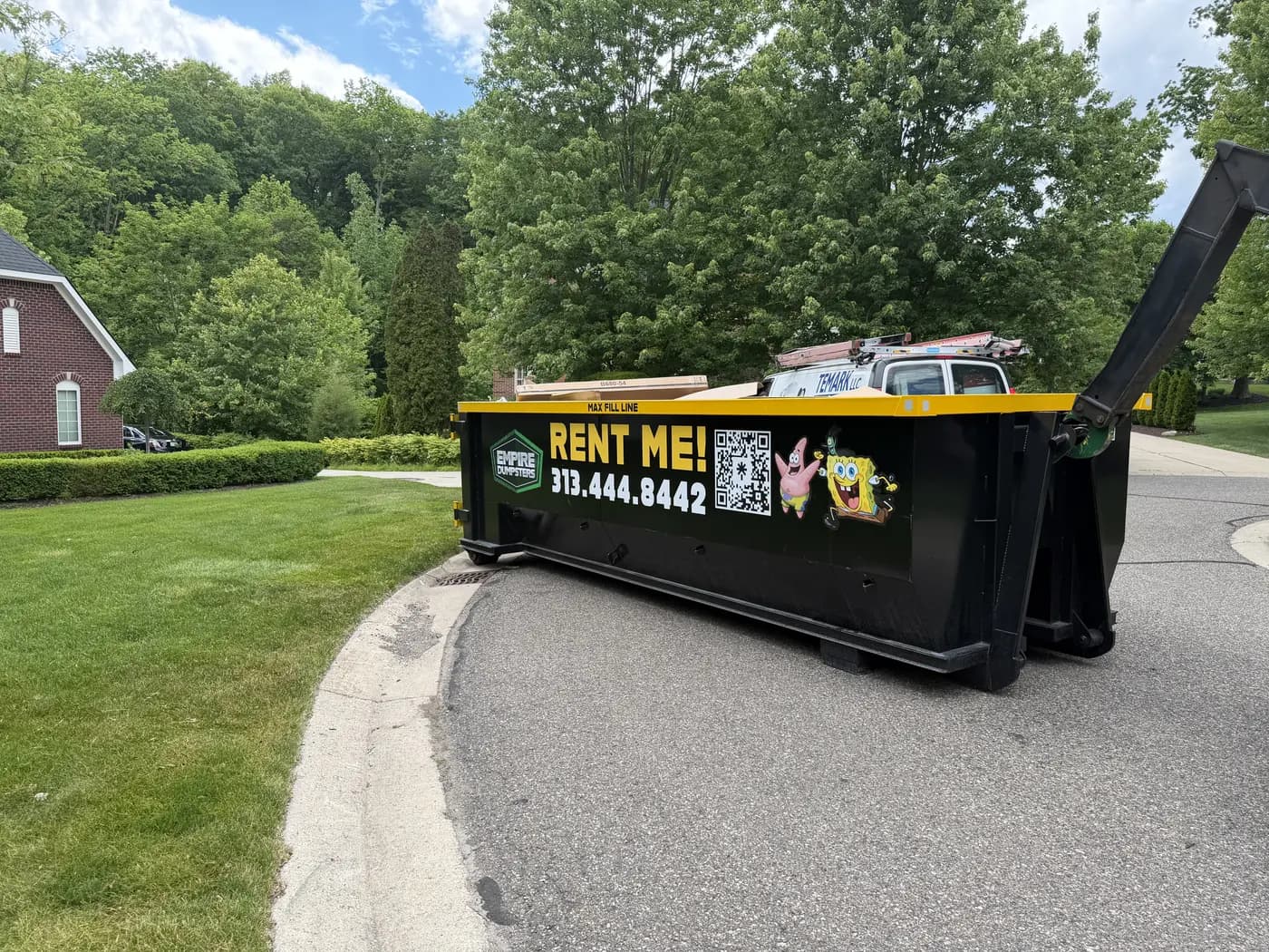 Black Empire Dumpsters roll-off with a yellow rail and a SpongeBob SquarePants wrap, set on a residential driveway