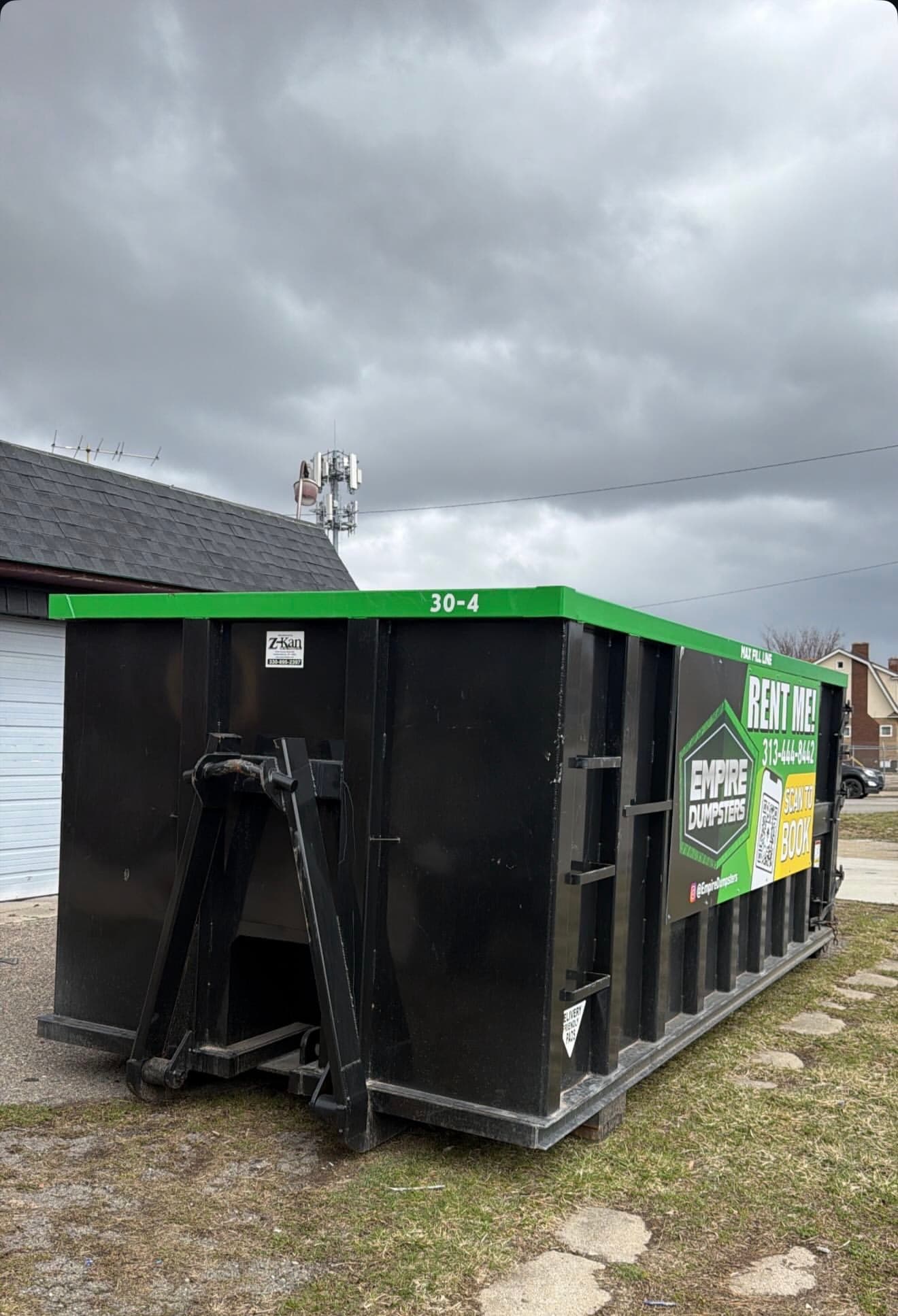 Black Empire Dumpsters roll-off container with green rails placed on a residential driveway