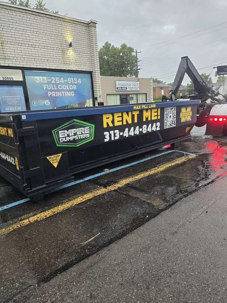 Black Empire Dumpsters roll-off with a blue rail and a Michigan Wolverines block M logo