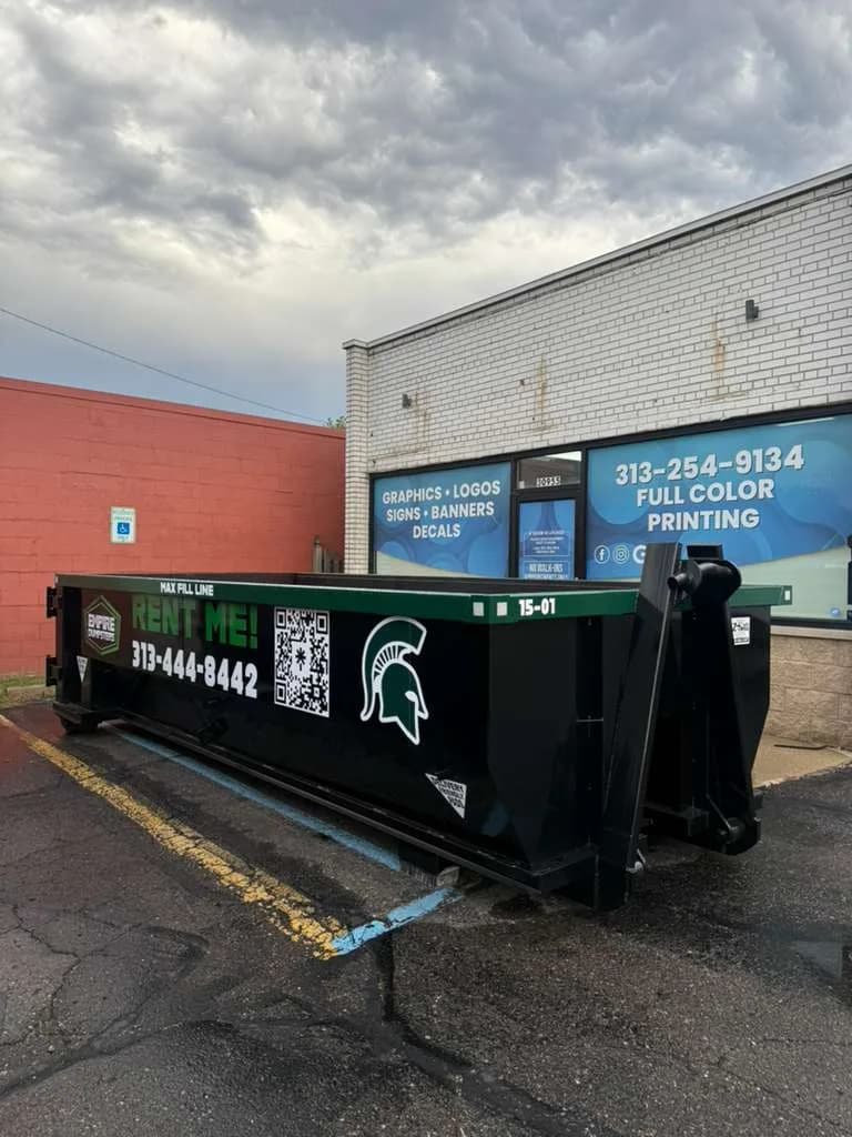 Black Empire Dumpsters roll-off with a green rail and a Michigan State Spartans helmet logo